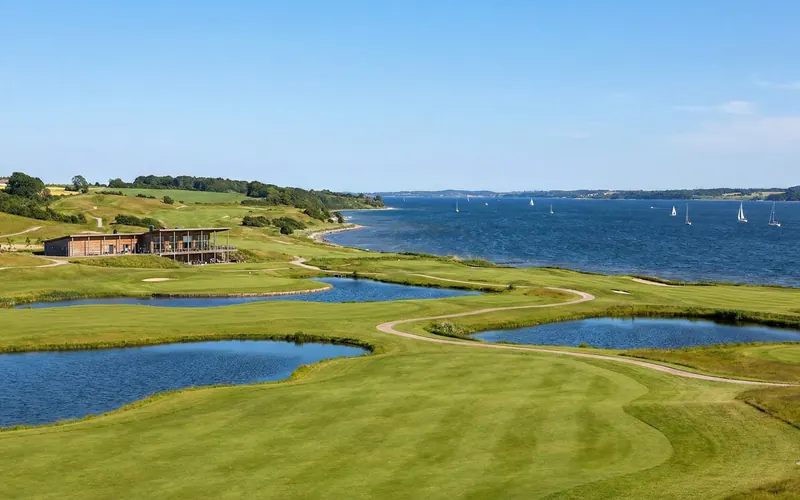 Golfklubben Storstrømmen mit Wasserhindernissen, Klubhaus und Blick auf den Guldborgsund mit Segelbooten