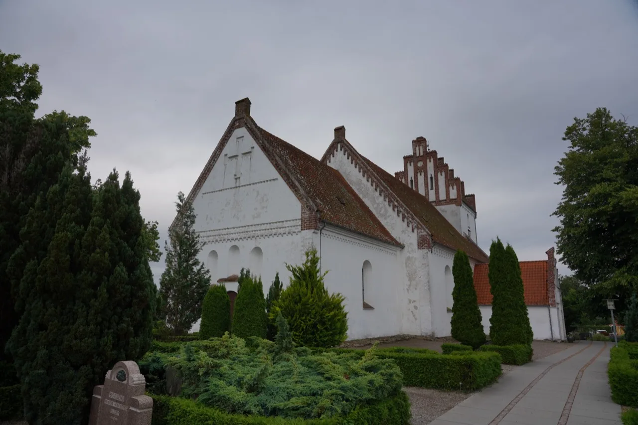 Idestrup Kirke – weiß getünchte romanische Dorfkirche mit rotem Ziegeldach, Staffelgiebel und kurz geschnittenen Eibenhecken auf dem Friedhof