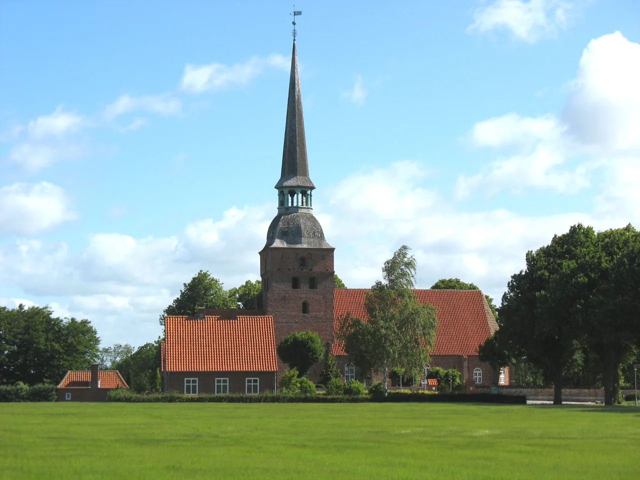 Kippinge Kirke aus rotem Backstein mit spitzem Laternenturm, umgeben von grünen Feldern in Nordwestfalster