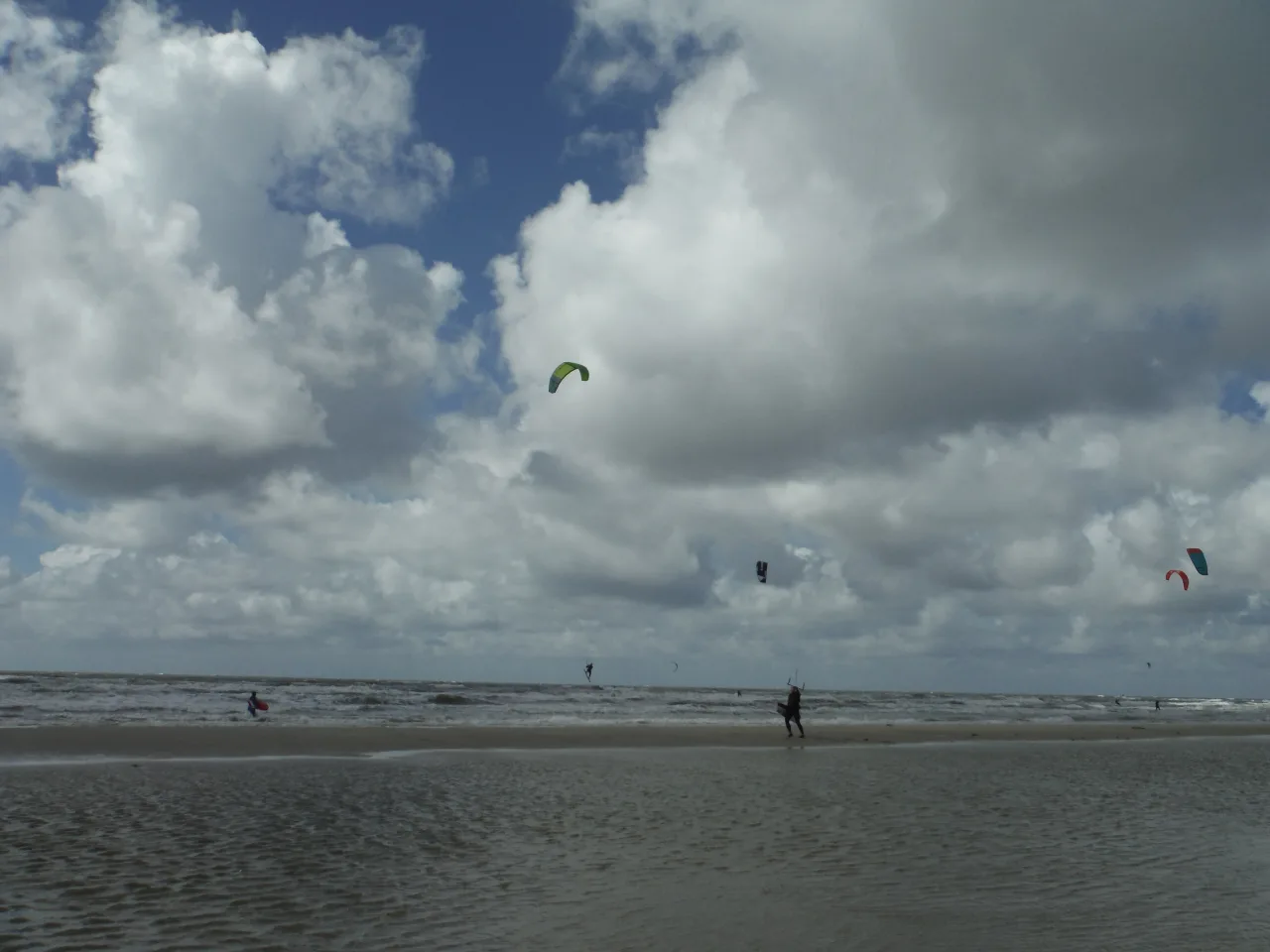 Kitesurfer mit grünem Schirm in der Luft über einer breiten dänischen Sandbank, leichter Schwell und ziehende Wolken