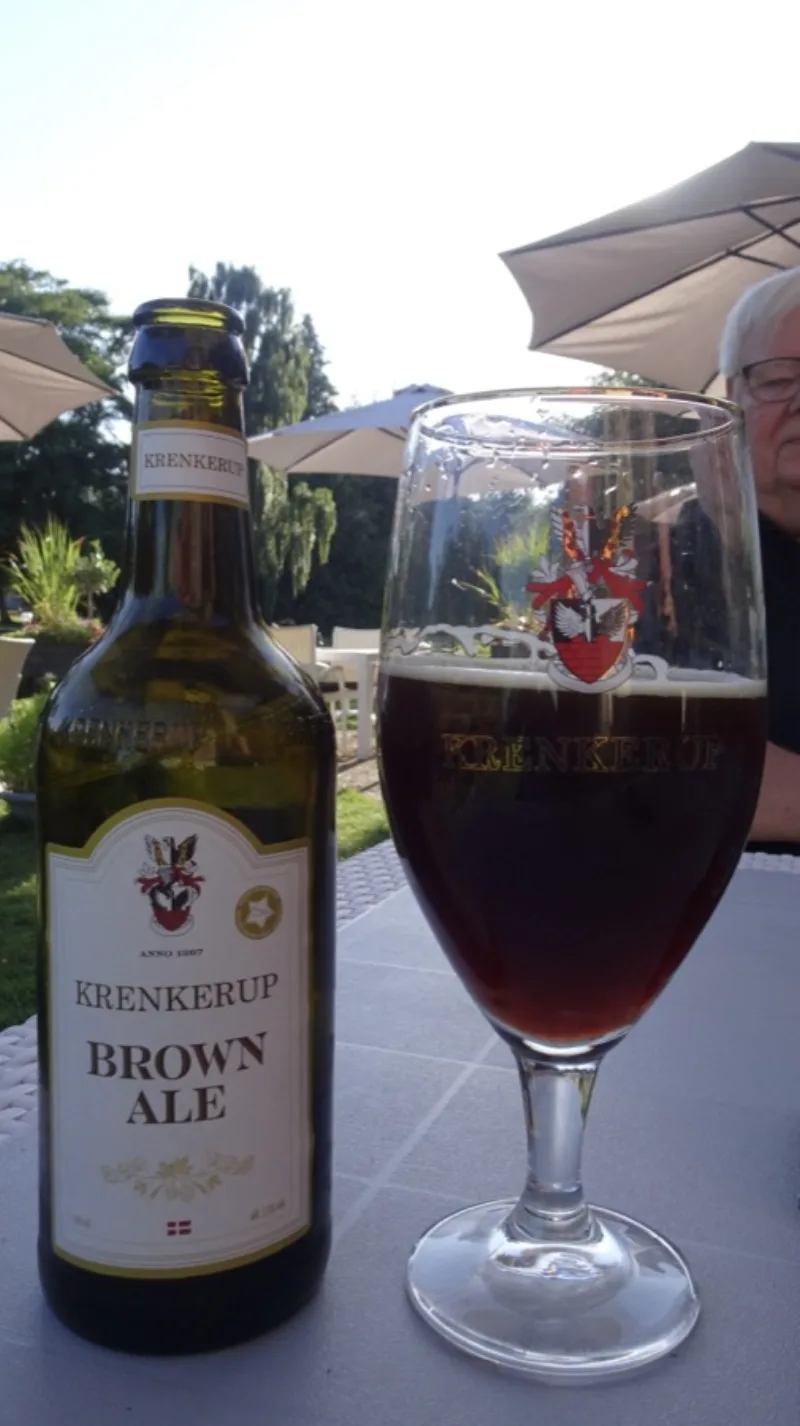Ein Glas Krenkerup Brown Ale neben der Flasche im Biergarten