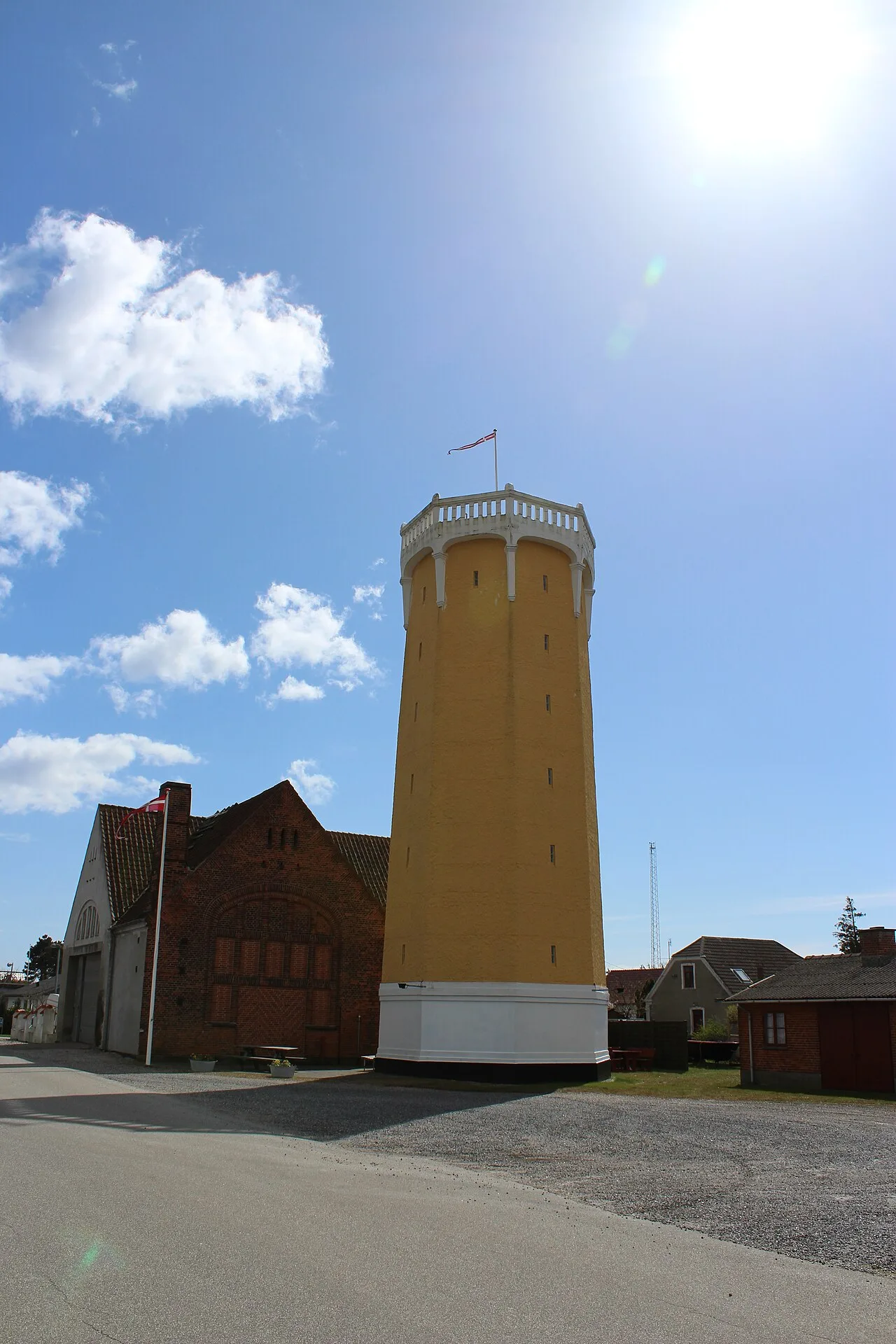 Gelber achteckiger Wasserturm von Gedser mit weißer Aussichtsgalerie und dänischer Flagge vor blauem Himmel